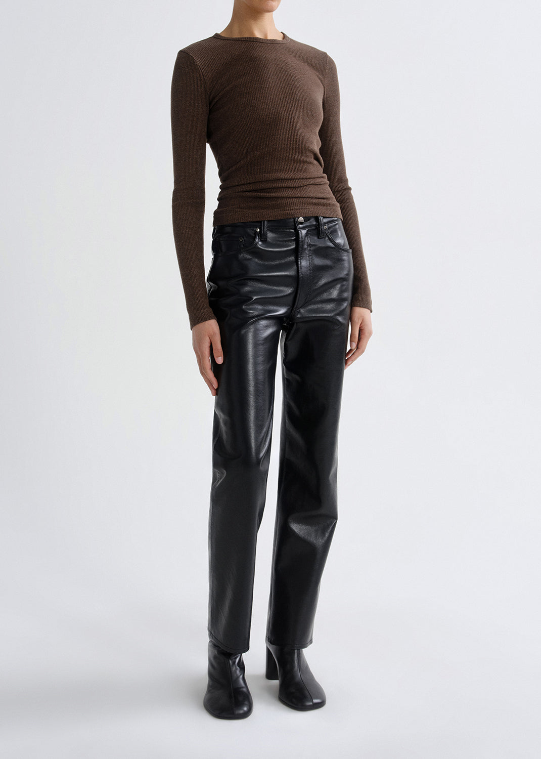 Person wearing a brown long sleeve ribbed top with black leather pants on a grey background.