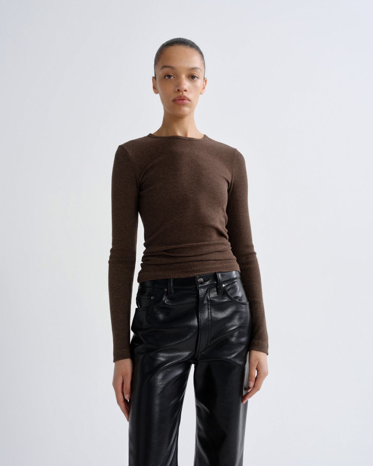 Person wearing a brown long-sleeve top and black leather pants on a white background