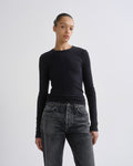 A model wearing a dark charcoal long-sleeve crewneck sweater and dark gray jeans, standing against a light gray studio background.
