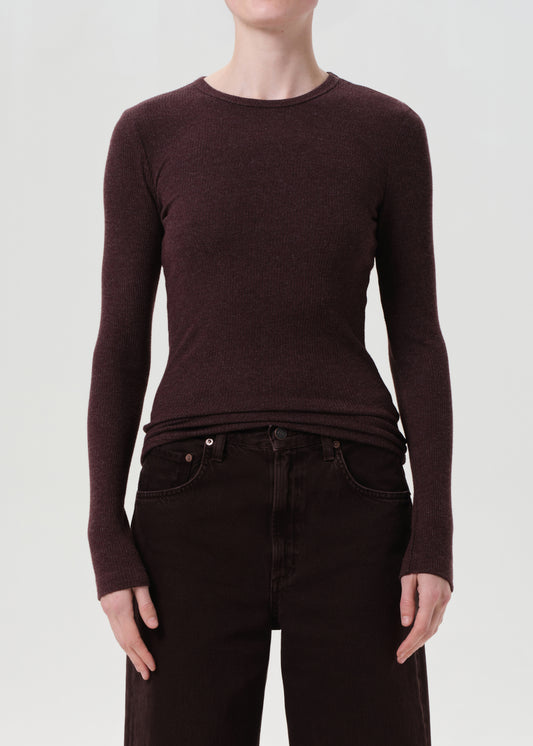 Person wearing a brown long-sleeve top and dark jeans on a white background