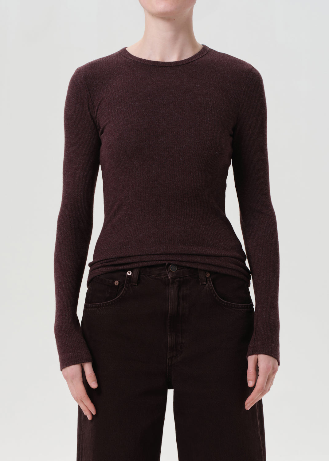 Person wearing a brown long-sleeve top and dark jeans on a white background