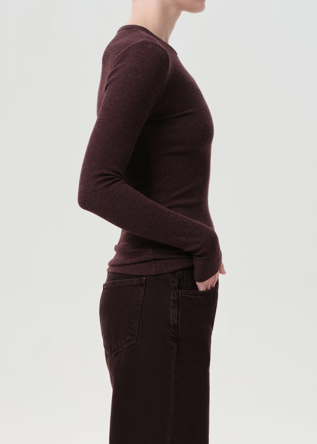 Person wearing a brown long-sleeve top and dark pants on a light gray background