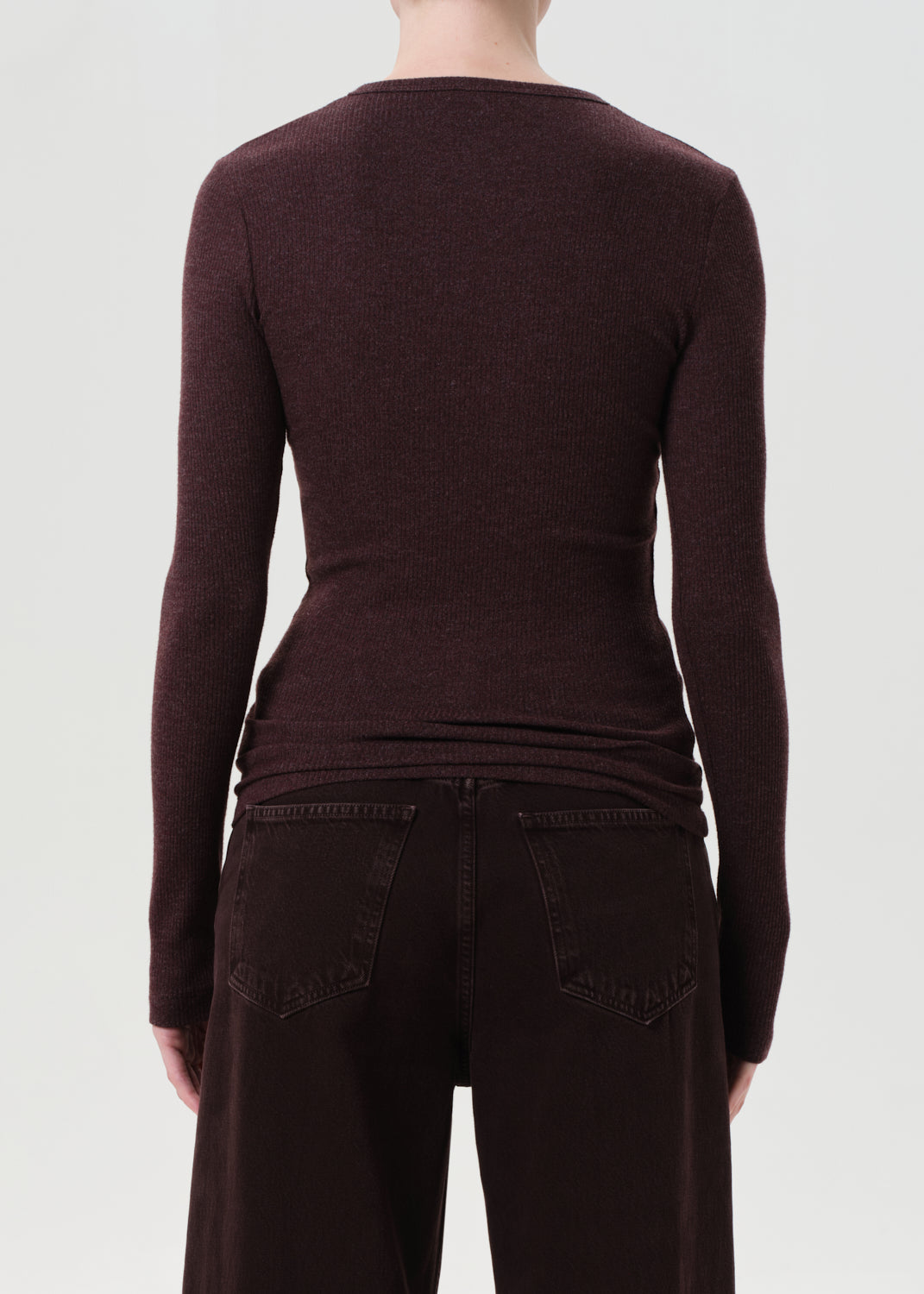 Person wearing a dark brown long-sleeve top and dark jeans on a light gray background