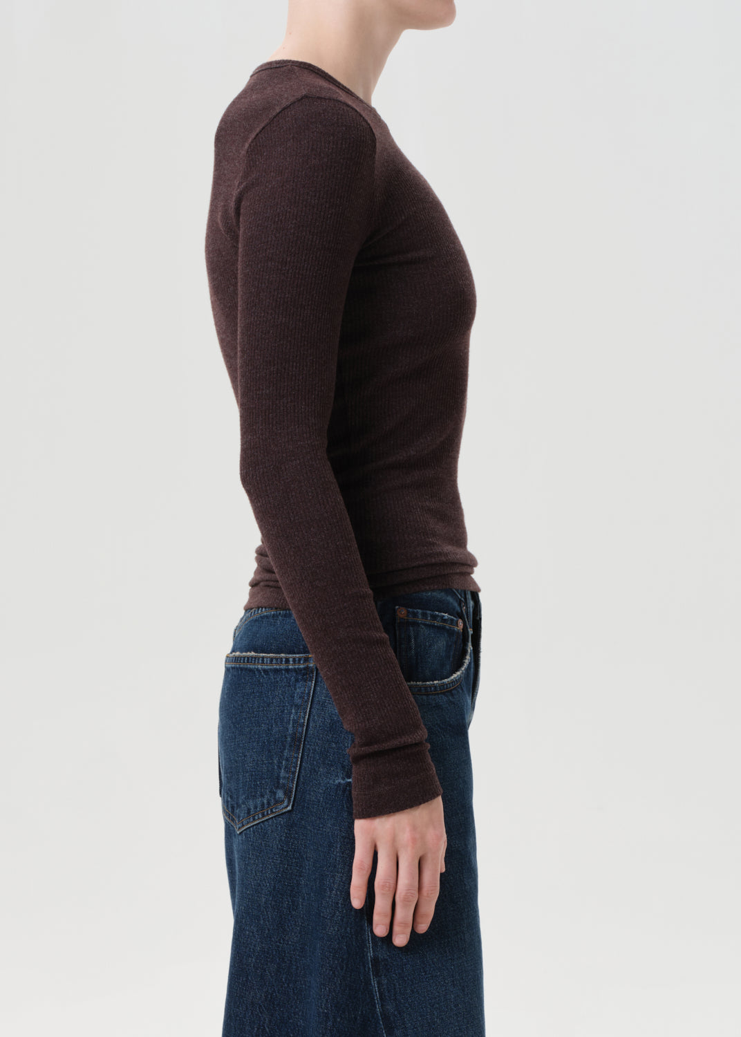Person wearing a brown long-sleeve shirt and blue jeans on a light gray background