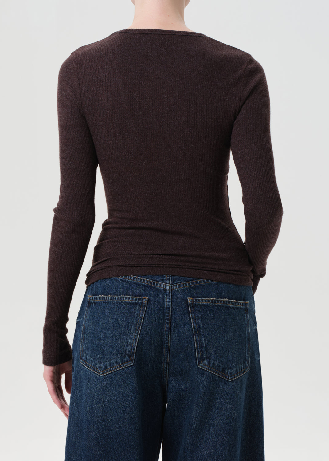 Person wearing a brown long-sleeve shirt and blue jeans on a white background
