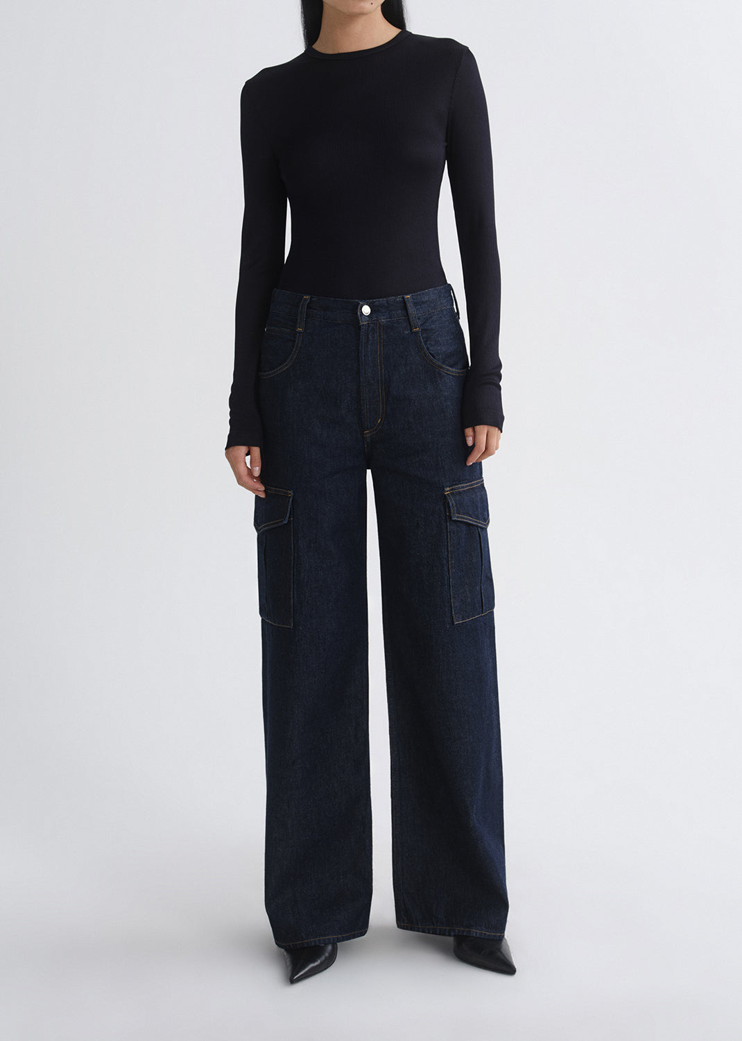 A model wearing a black long-sleeve top and dark blue wide-leg cargo jeans with flap pockets, standing against a grey background.