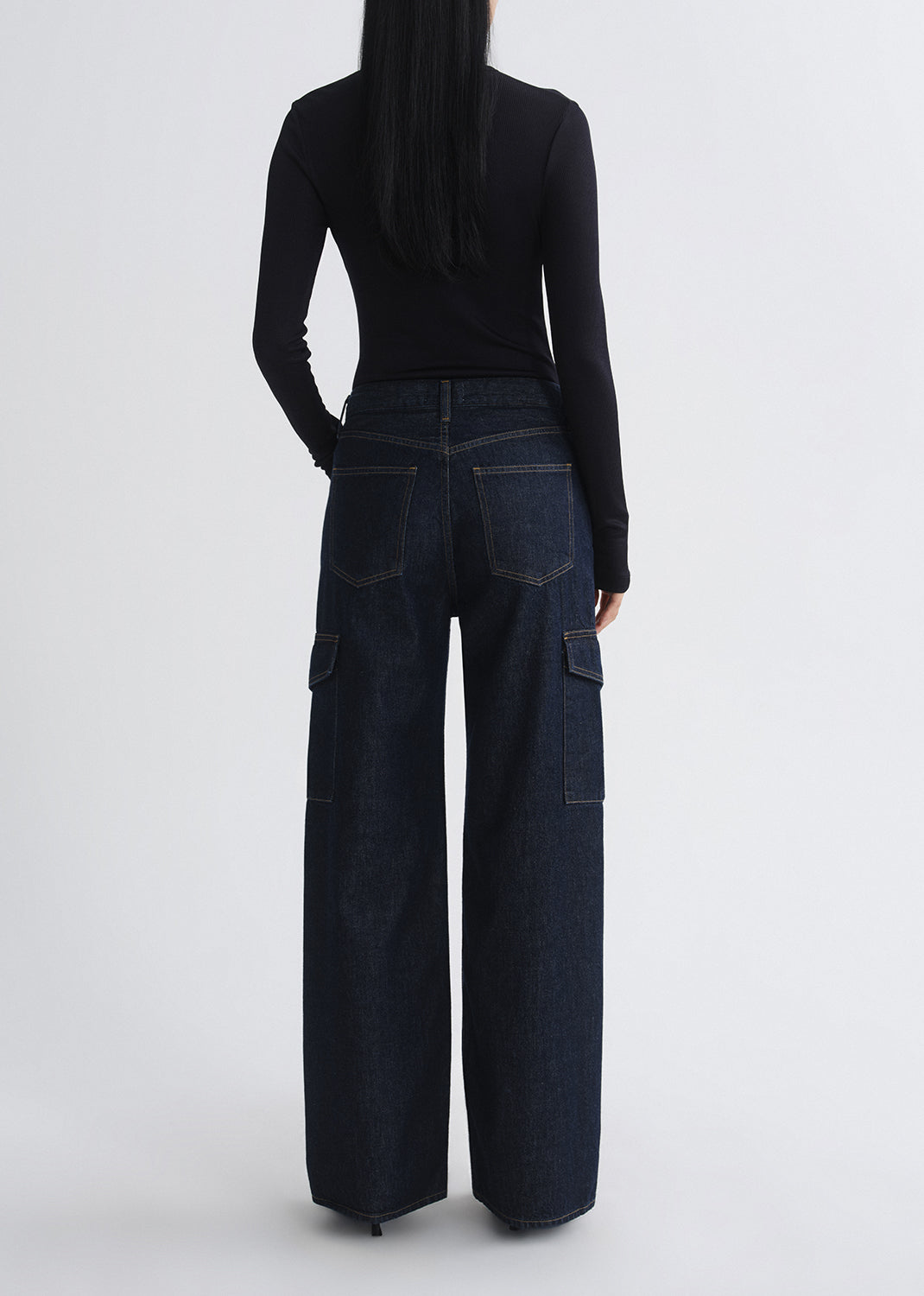 A model shown from the back wearing dark wash wide-leg cargo jeans and a black long-sleeve top against a grey background.
