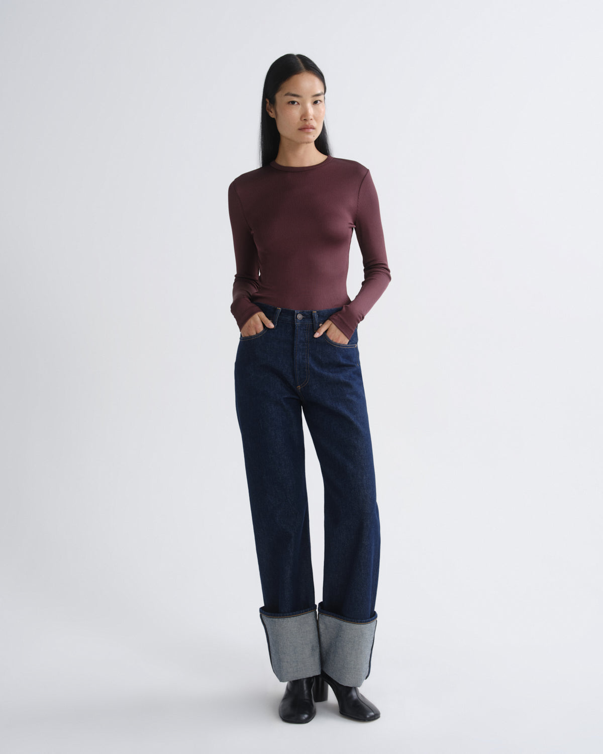 Person wearing a burgundy top and dark blue jeans on a white background