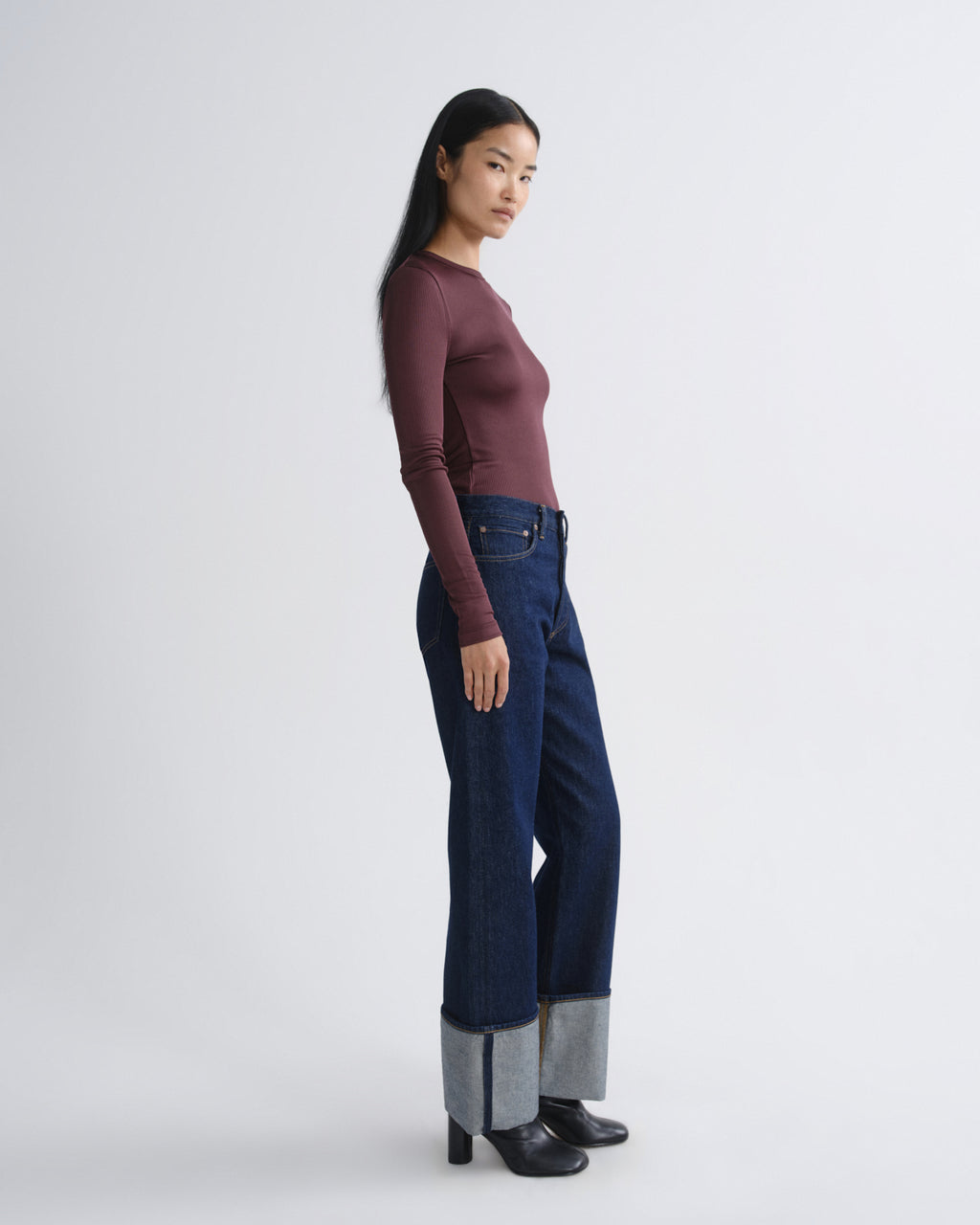 Woman wearing a maroon long-sleeve top and dark blue jeans on a white background