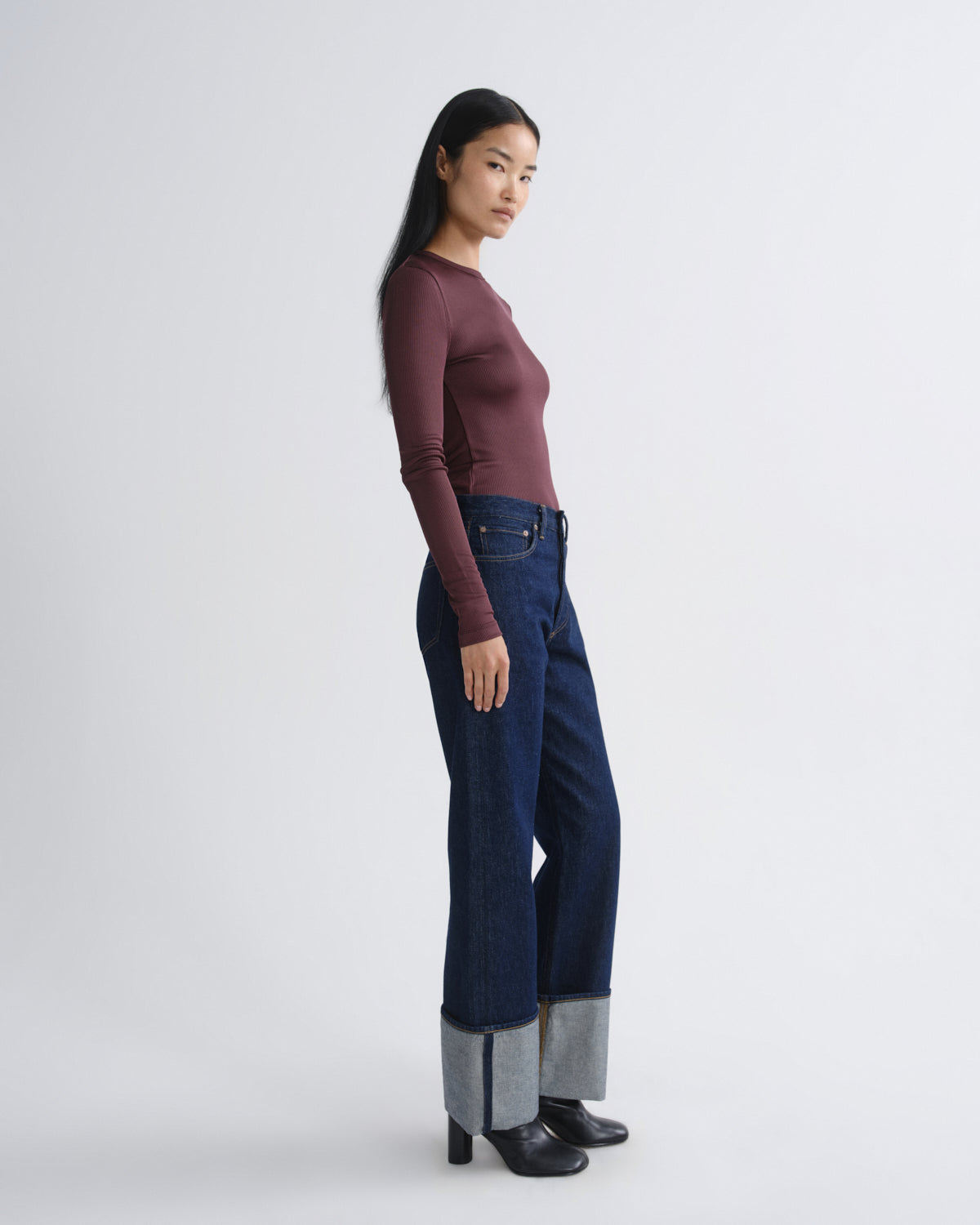 Woman wearing a maroon long-sleeve top and dark blue jeans on a white background