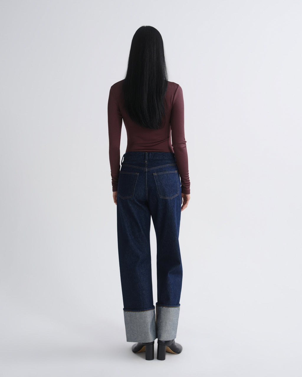 Person wearing dark blue jeans with gray cuffs on a white background
