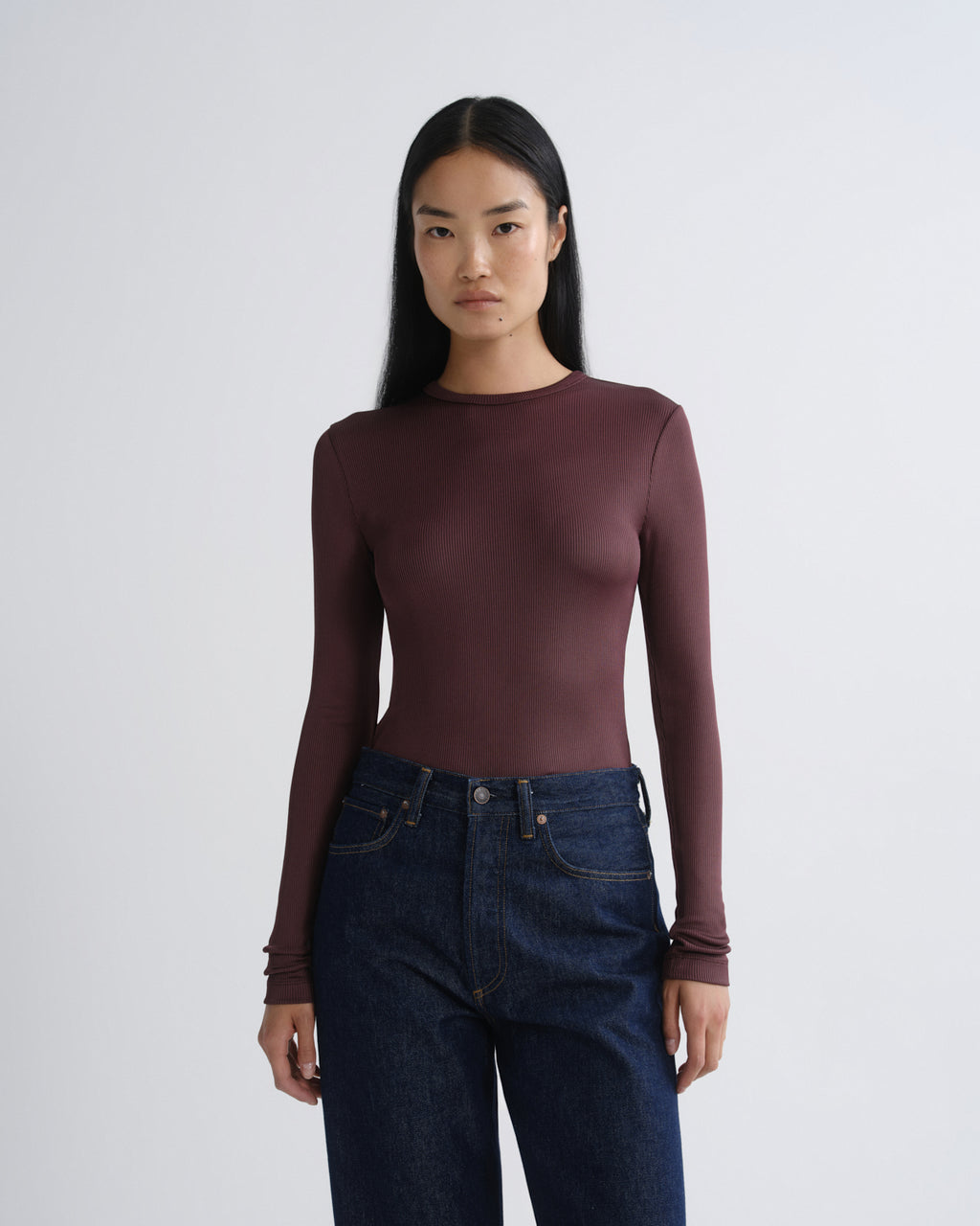 Person wearing a maroon long-sleeve top and blue jeans on a white background