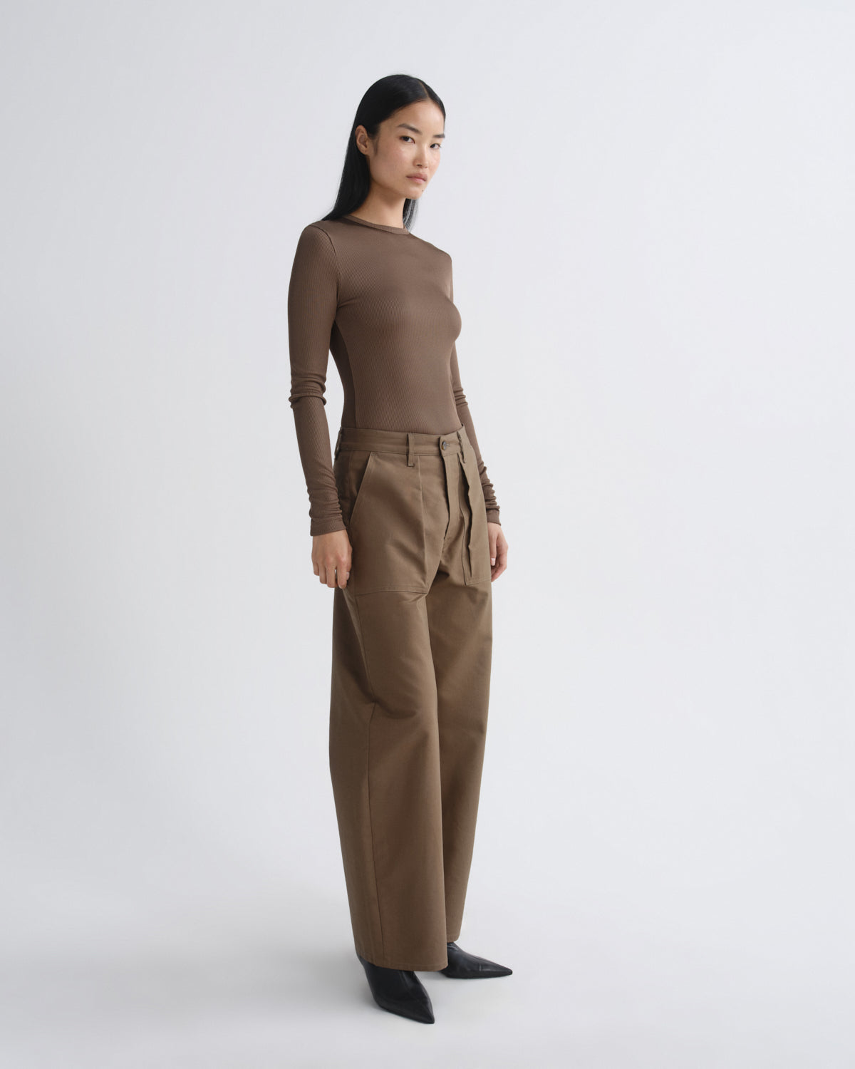 Woman wearing a brown long-sleeve top and beige pants on a white background