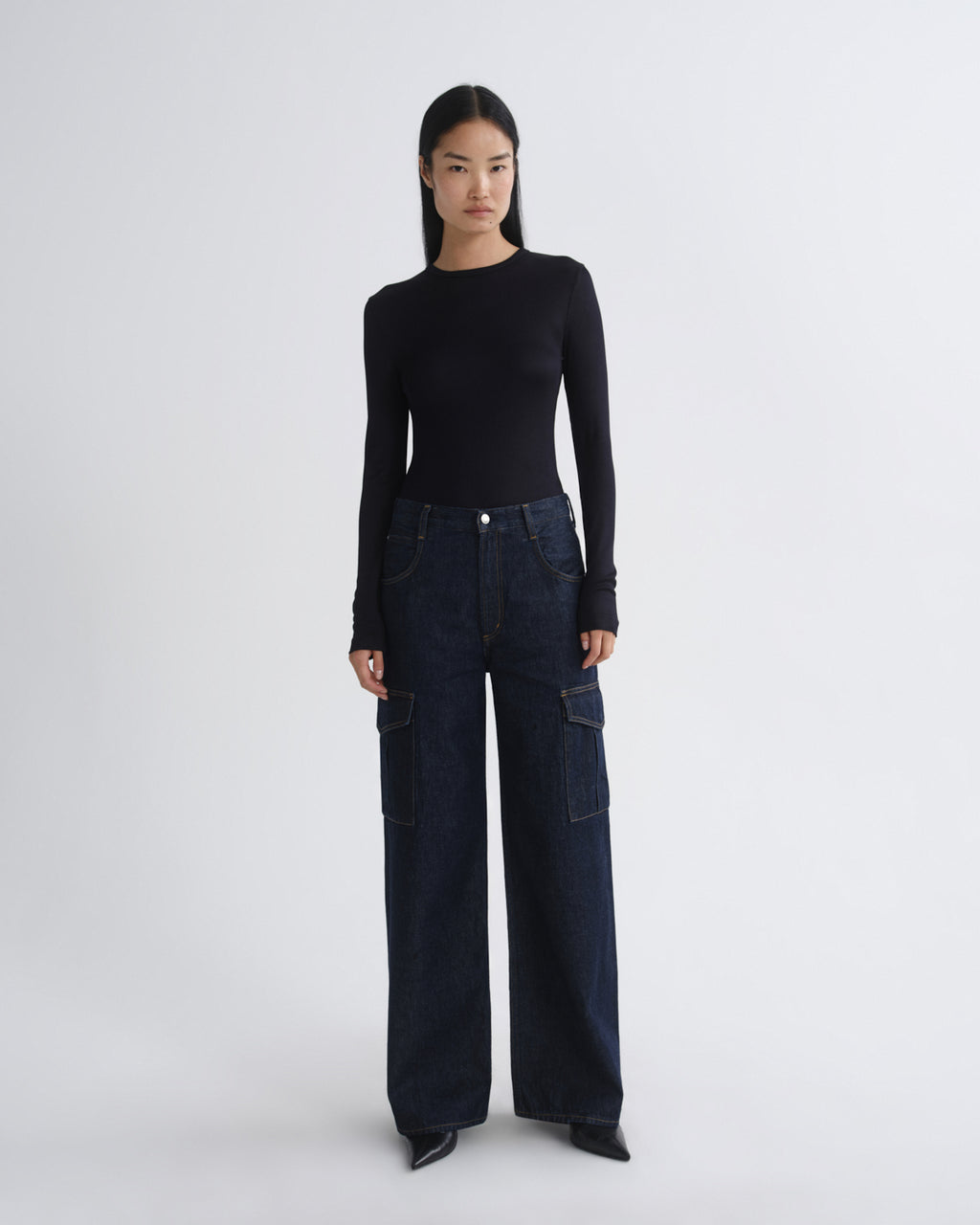 Person wearing a black long-sleeve top and dark blue wide-leg jeans on a white background