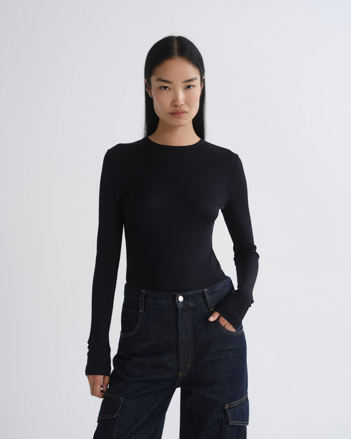 Person wearing a black long-sleeve top and dark jeans on a white background