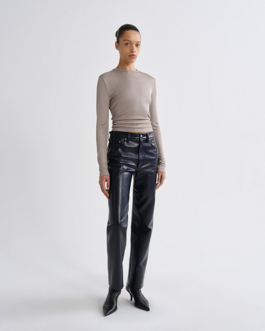 Person wearing a beige long-sleeve top and black leather pants on a white background