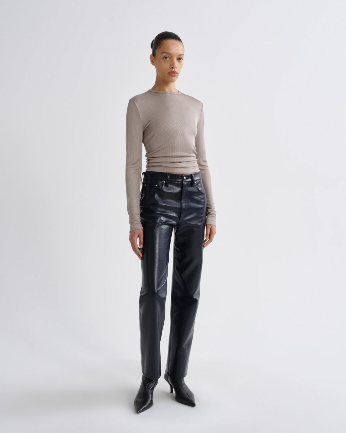 Person wearing a beige long-sleeve top and black leather pants on a white background