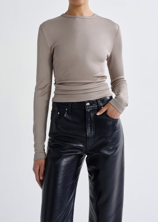 A model wearing a beige long-sleeve ribbed knit top tucked into black faux-leather wide-leg pants, shown from the neck down against a grey background.