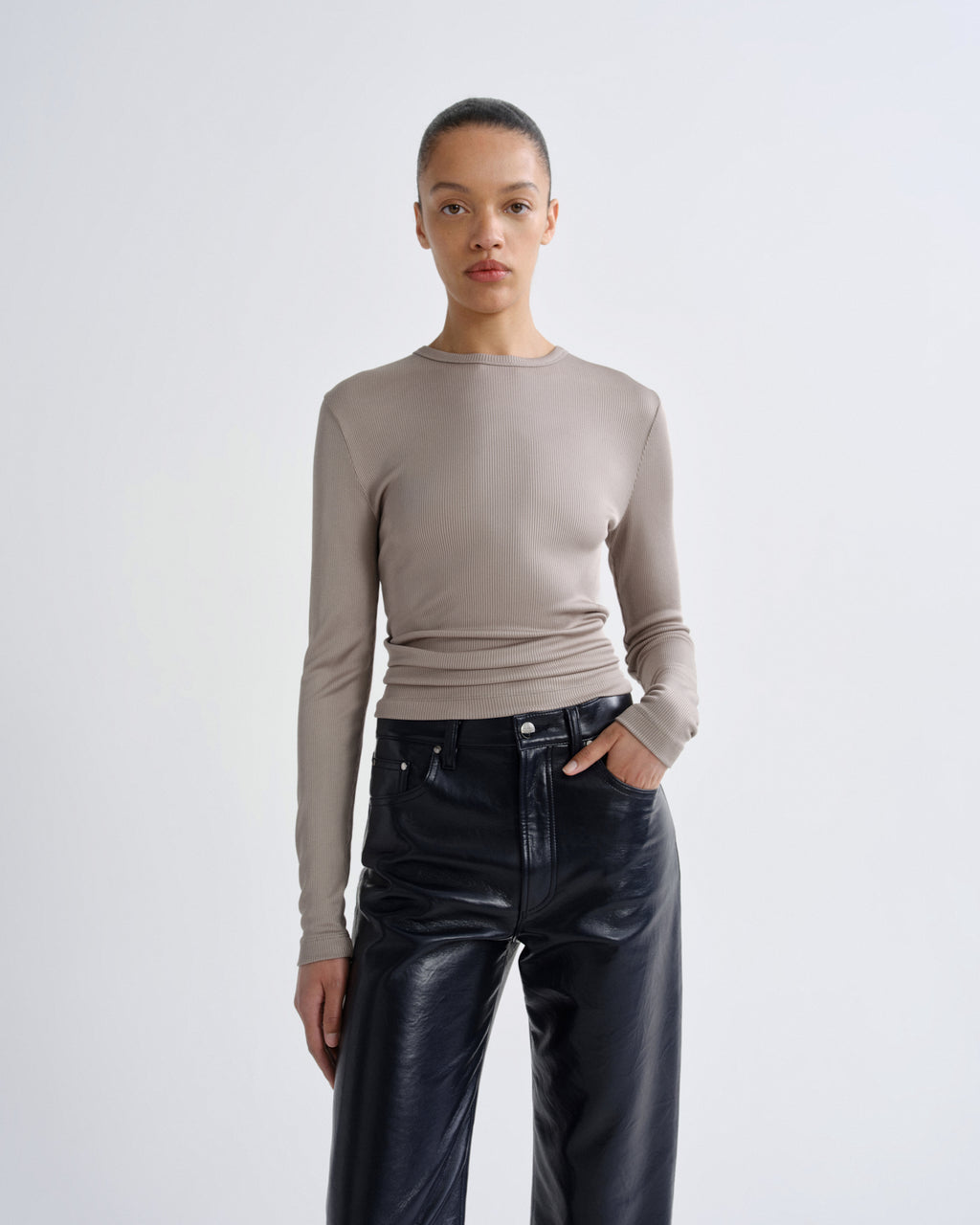 Person wearing a beige long-sleeve top and black leather pants on a white background