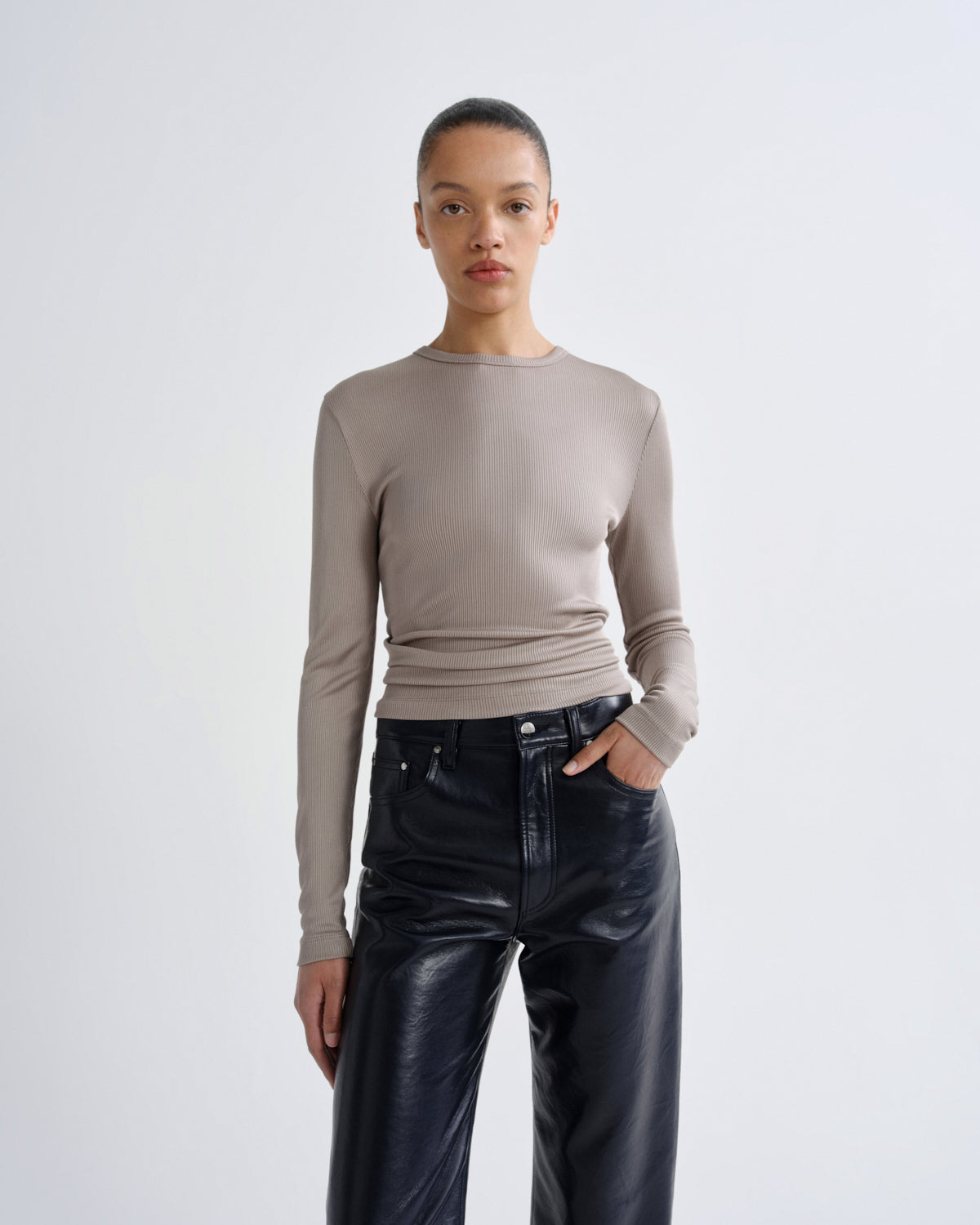 Person wearing a beige long-sleeve top and black leather pants on a white background