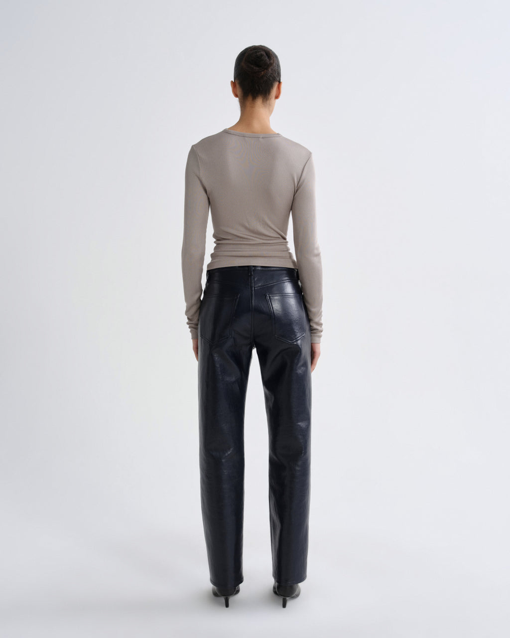 Person wearing a beige long-sleeve top and dark blue leather pants on a white background