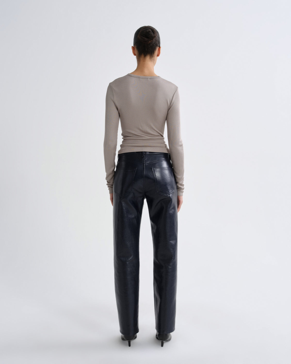 Person wearing a beige long-sleeve top and dark blue leather pants on a white background