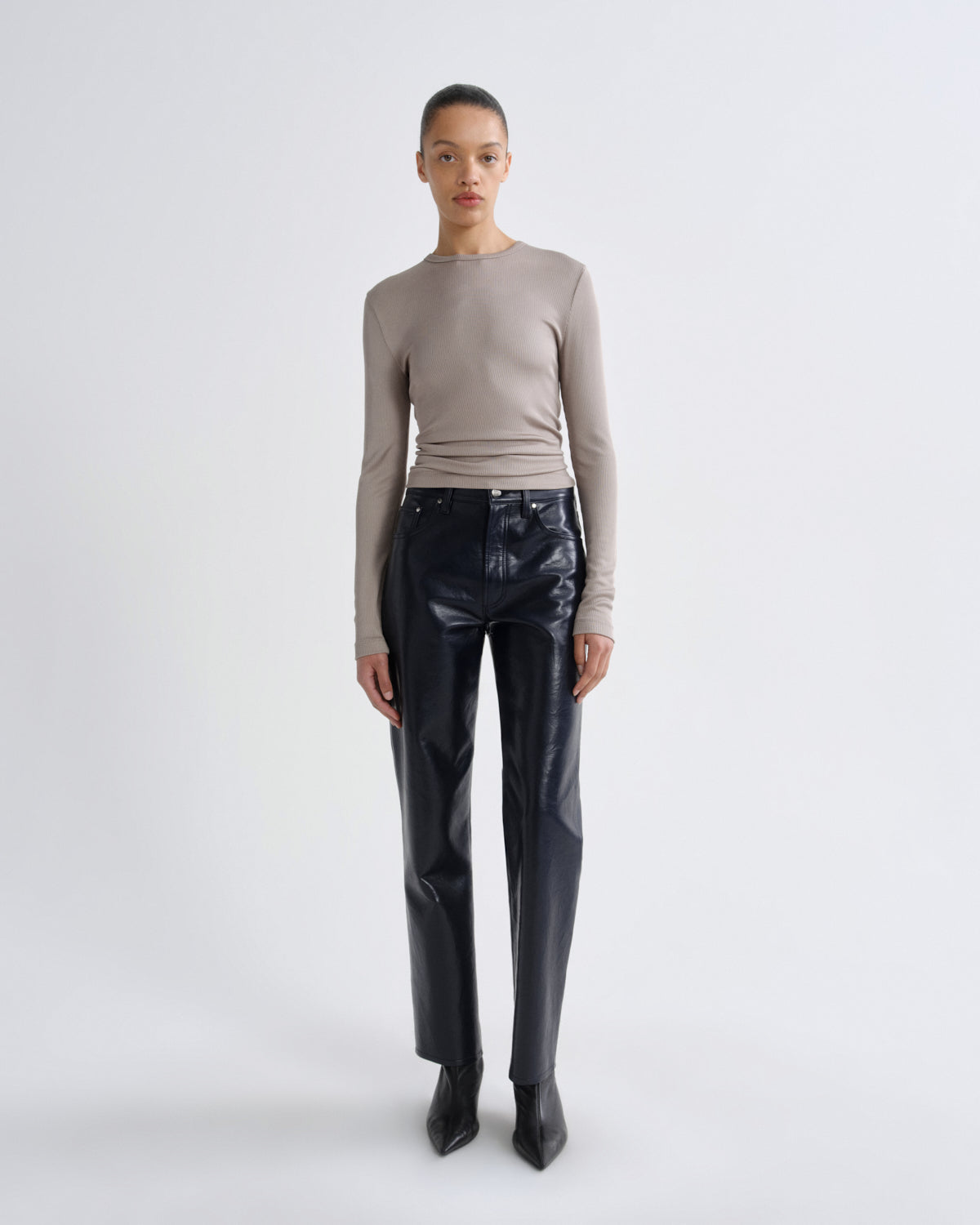 Person wearing a beige long-sleeve top and black shiny pants on a white background
