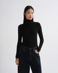 A model wearing a black long-sleeve mock neck turtleneck top and dark blue jeans, standing against a light gray studio background.