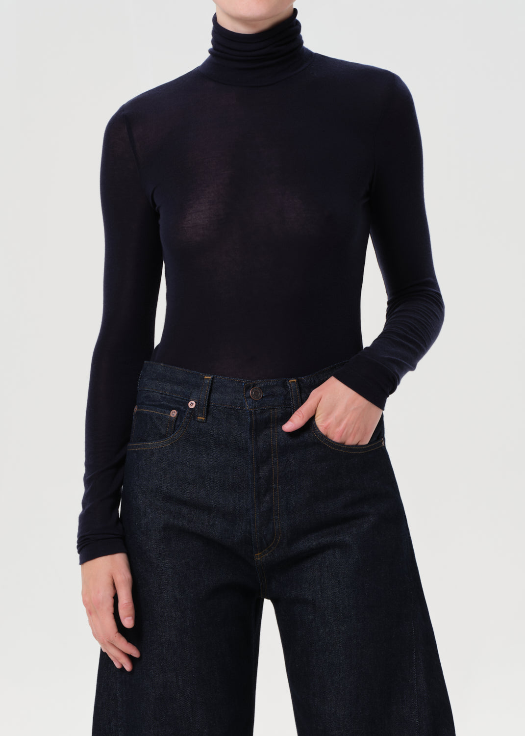 Person wearing a blue turtleneck and dark jeans on a white background
