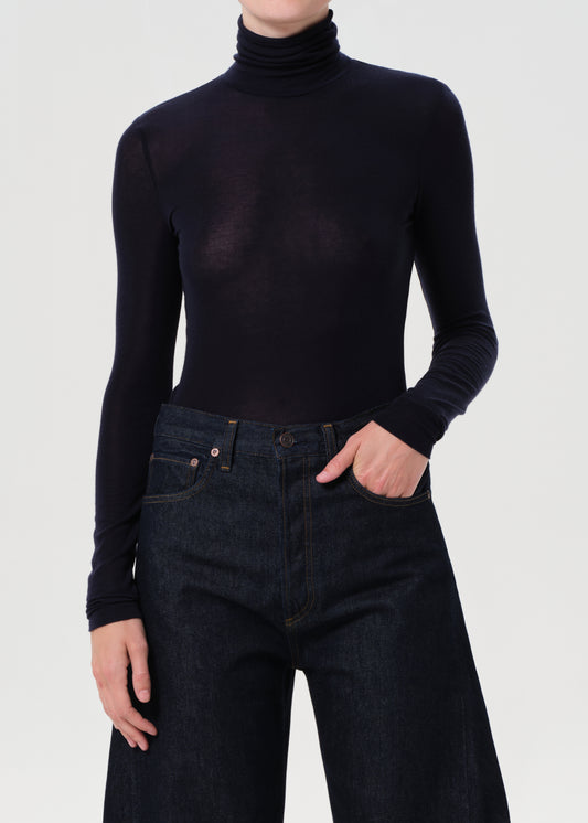 Person wearing a blue turtleneck and dark jeans on a white background