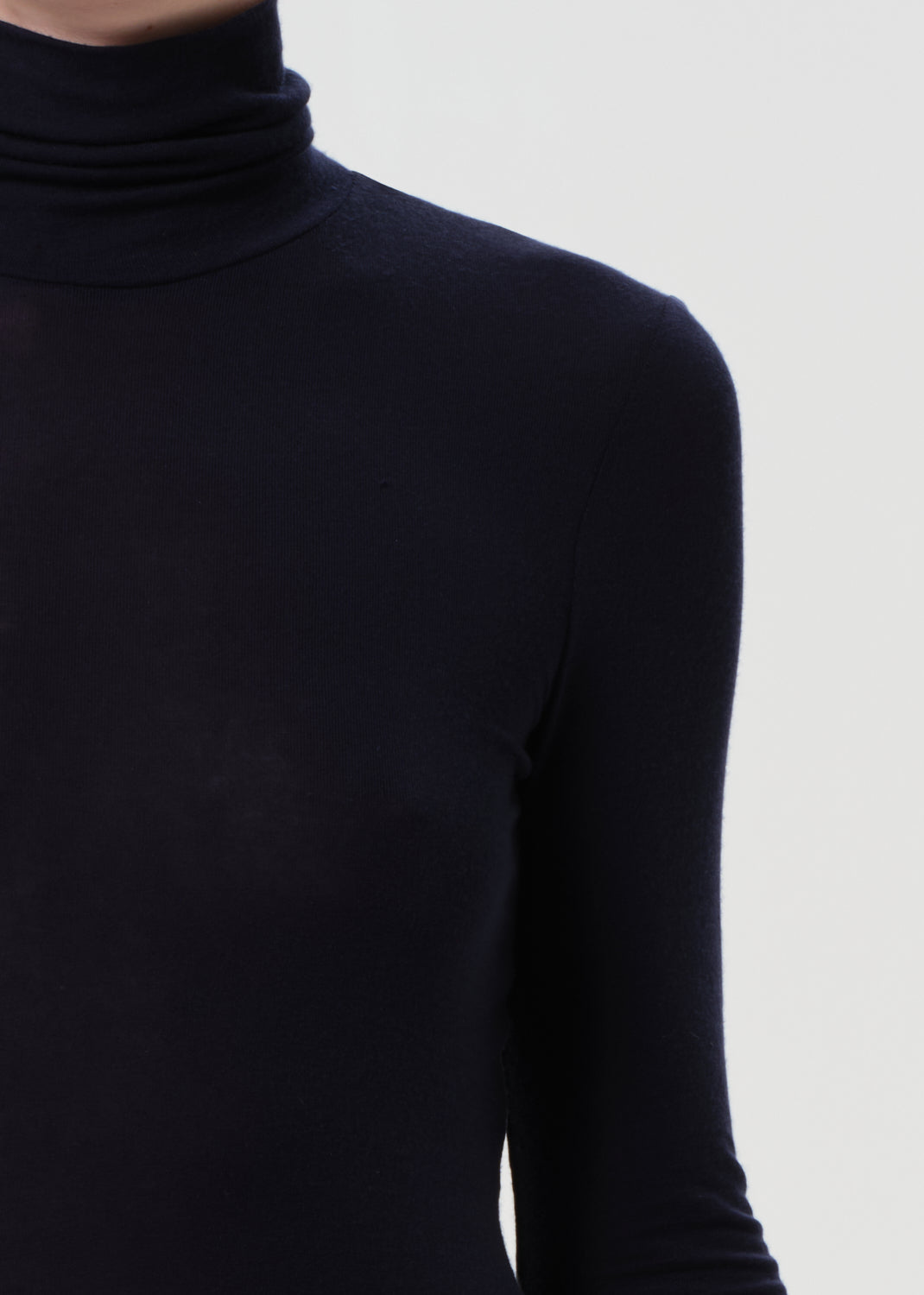 Person wearing a blue turtleneck and dark jeans on a white background