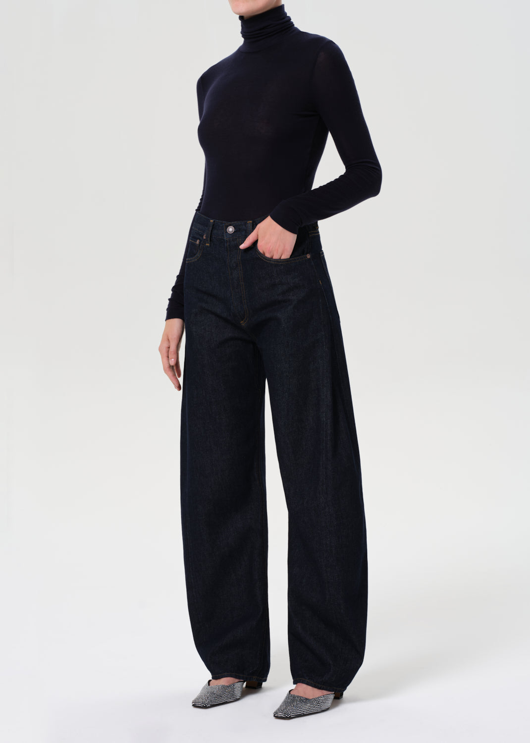 Person wearing a blue turtleneck and dark jeans on a white background