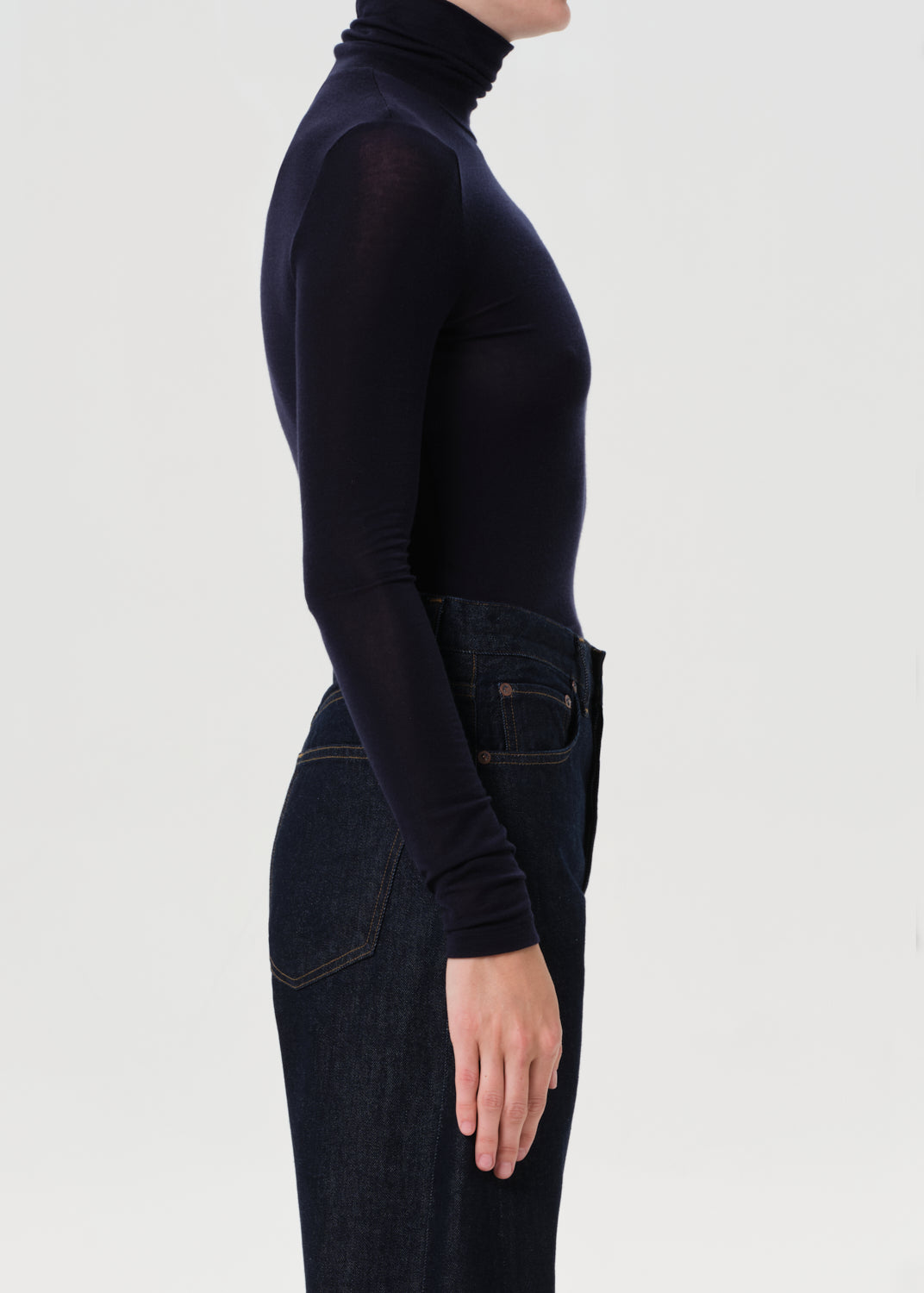 Person wearing a blue turtleneck and dark jeans on a white background