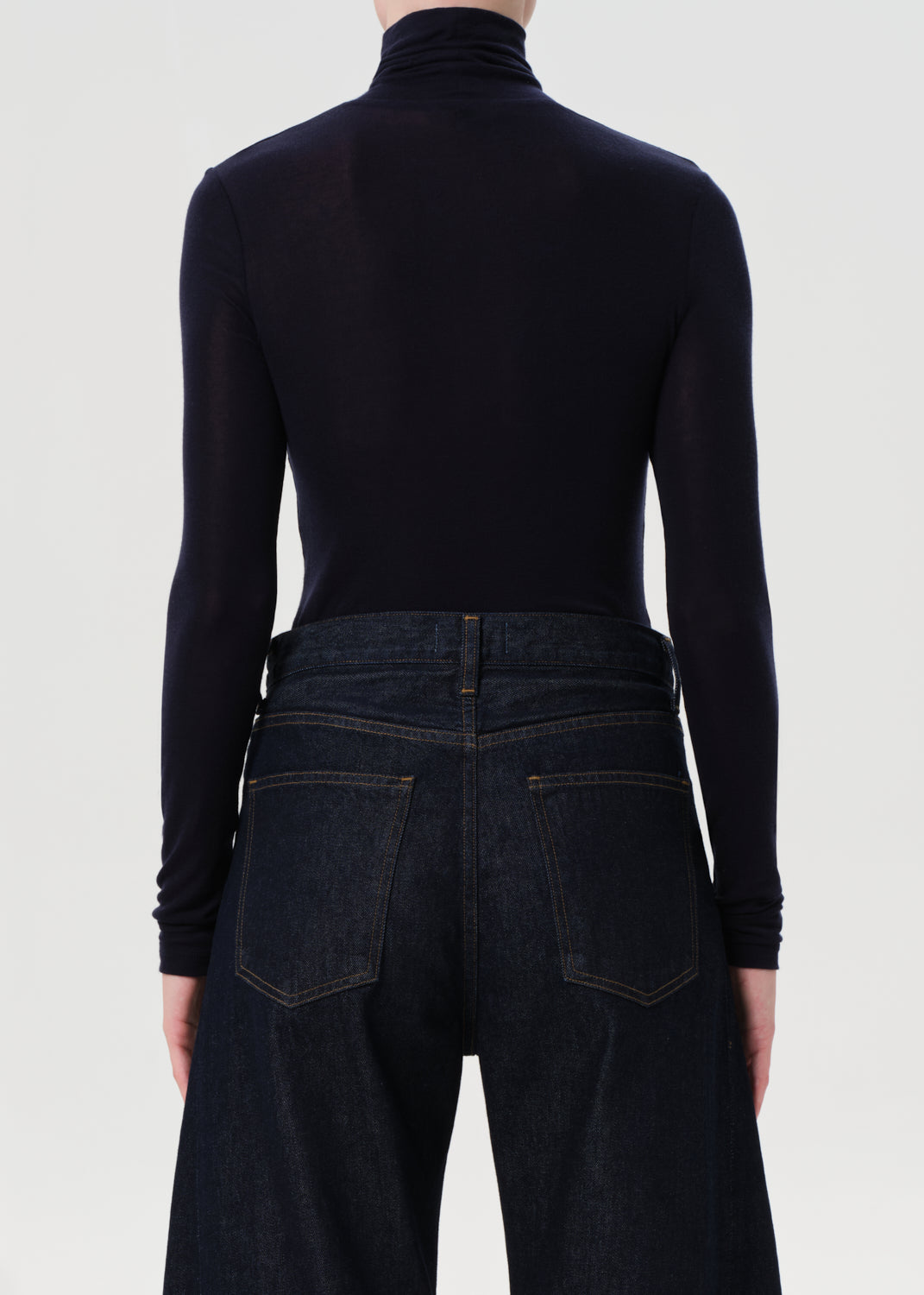 Person wearing a blue turtleneck and dark jeans on a white background