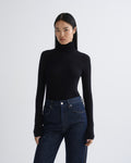A model wearing a black long-sleeve turtleneck top and dark blue jeans, standing against a light gray studio background.