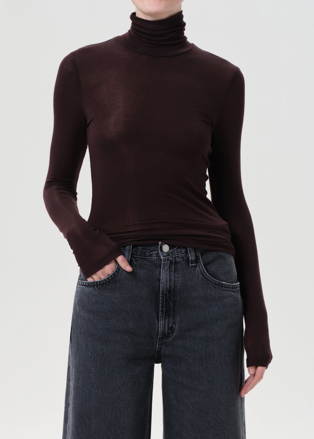 Person wearing a brown turtleneck sweater and dark jeans on a white background