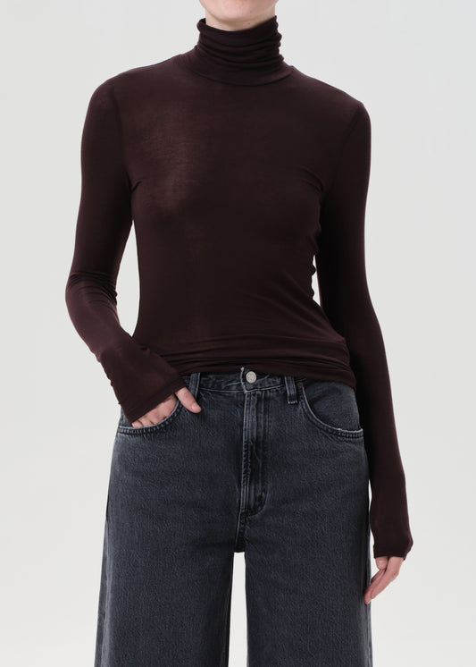 Person wearing a brown turtleneck sweater and dark jeans on a white background