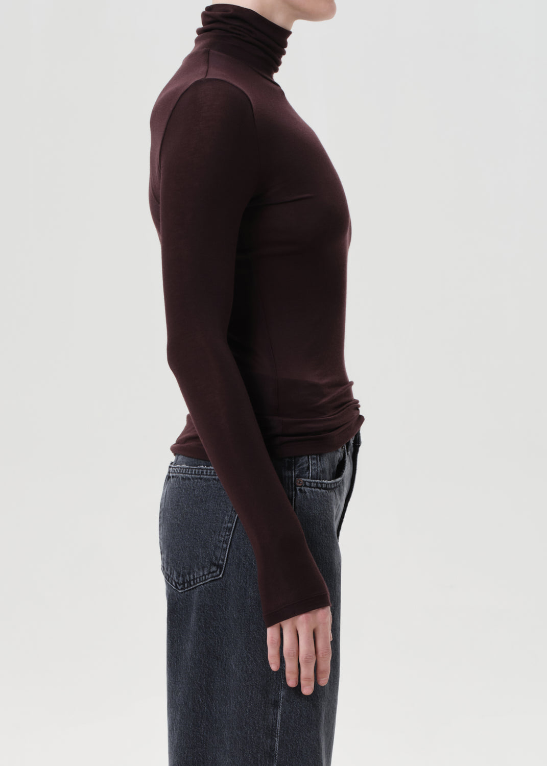 Person wearing a brown turtleneck and jeans on a light gray background