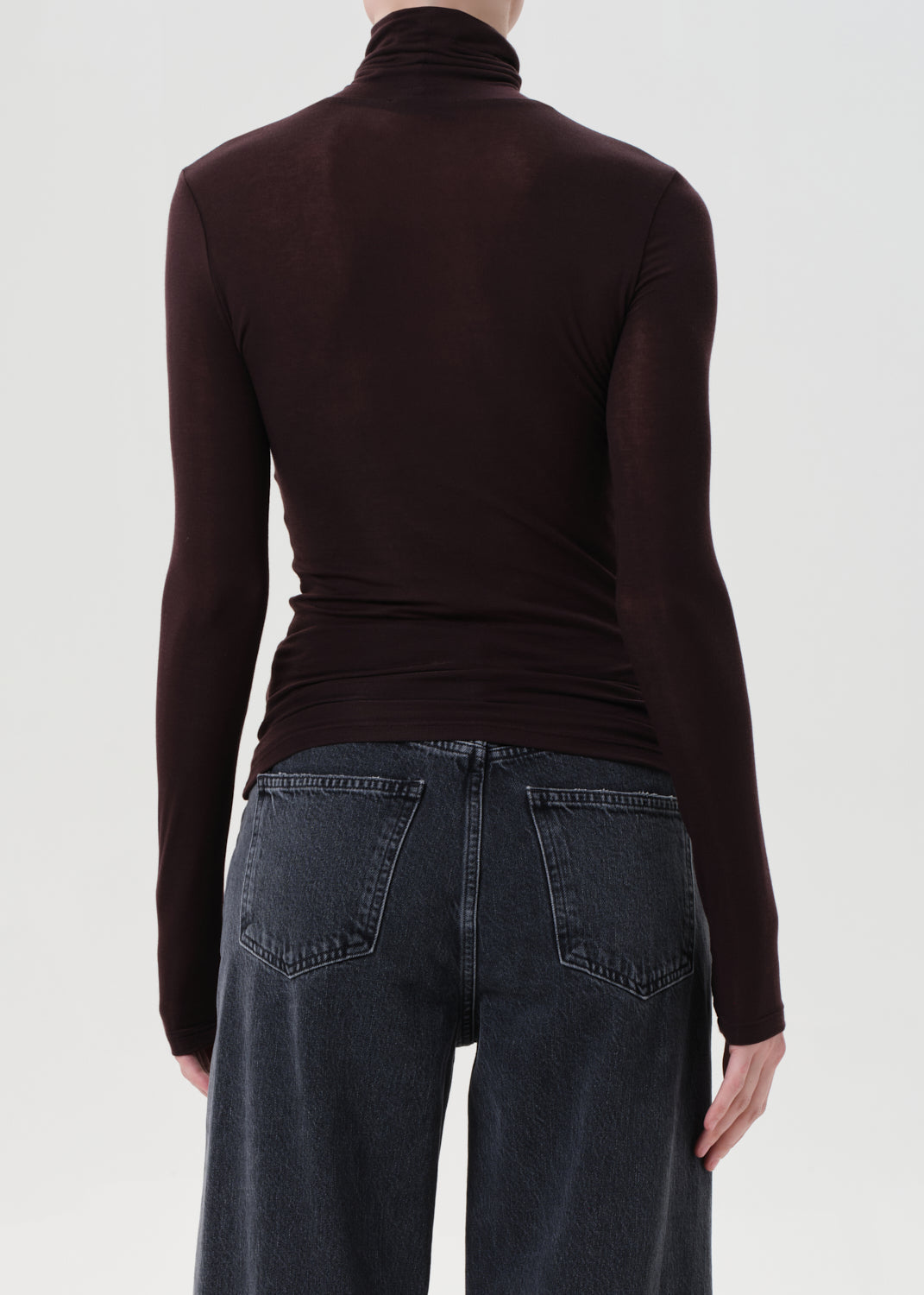 Person wearing a brown turtleneck and dark jeans on a white background