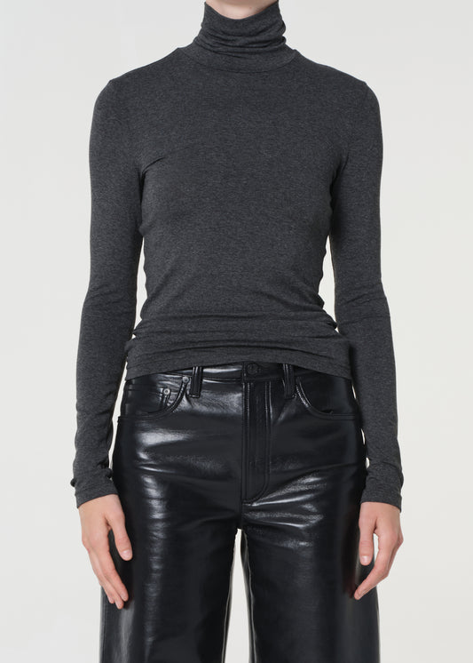 Person wearing a dark gray turtleneck sweater and black leather pants on a white background