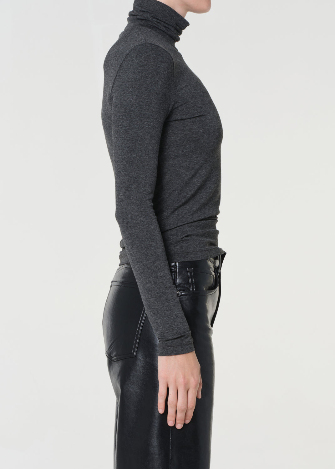 Person wearing a dark gray turtleneck sweater and black leather pants on a white background