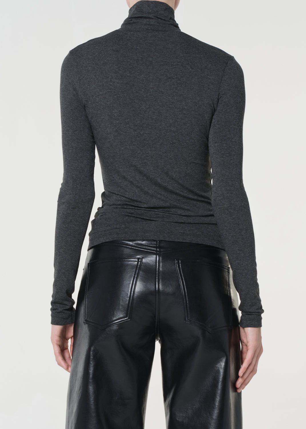 Person wearing a dark gray turtleneck sweater and black leather pants on a white background