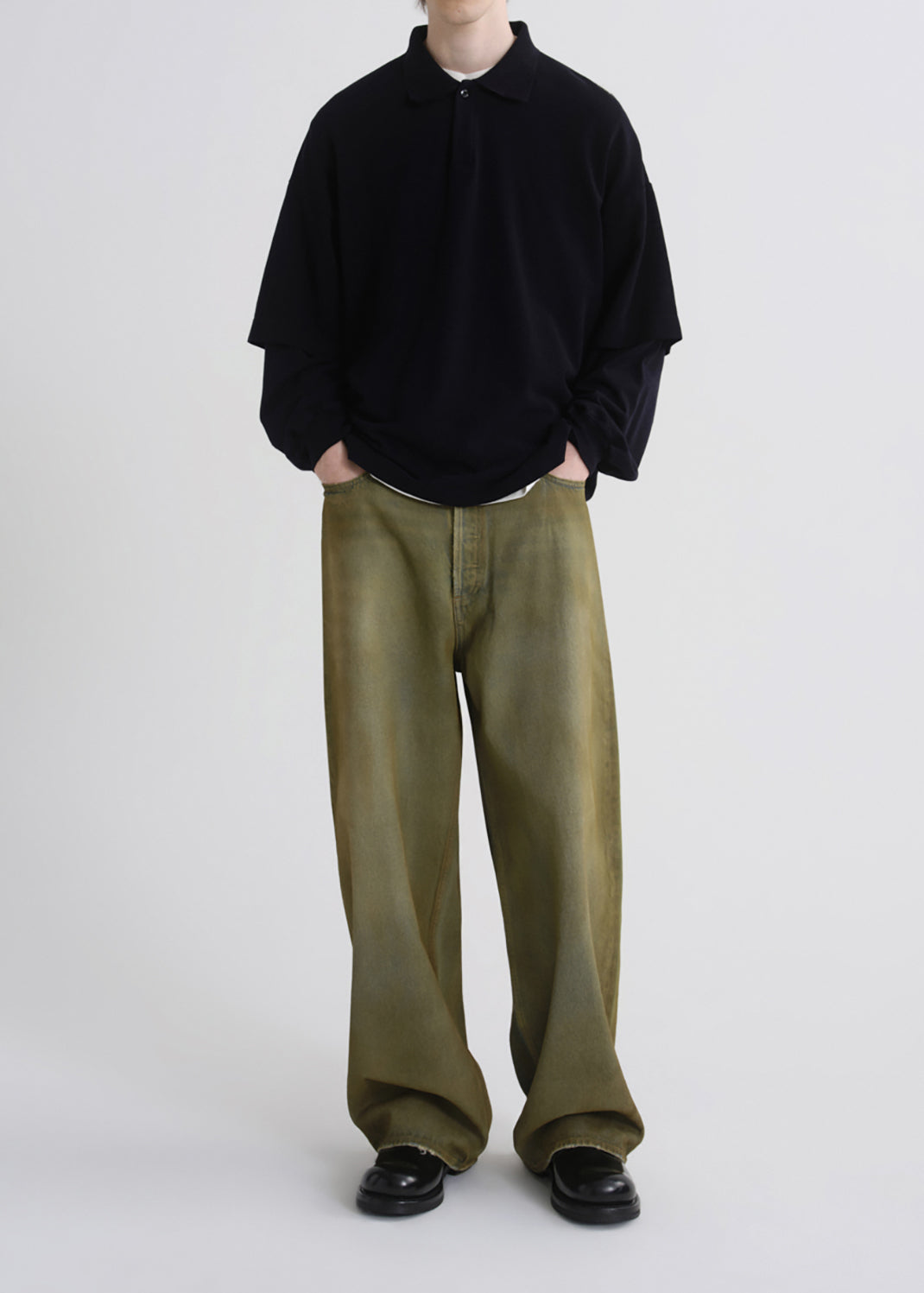 A model wearing an oversized black long-sleeve polo shirt and wide-leg olive green trousers, paired with black leather shoes, against a grey background.