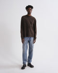 Man wearing a brown sweater and blue jeans on a white background
