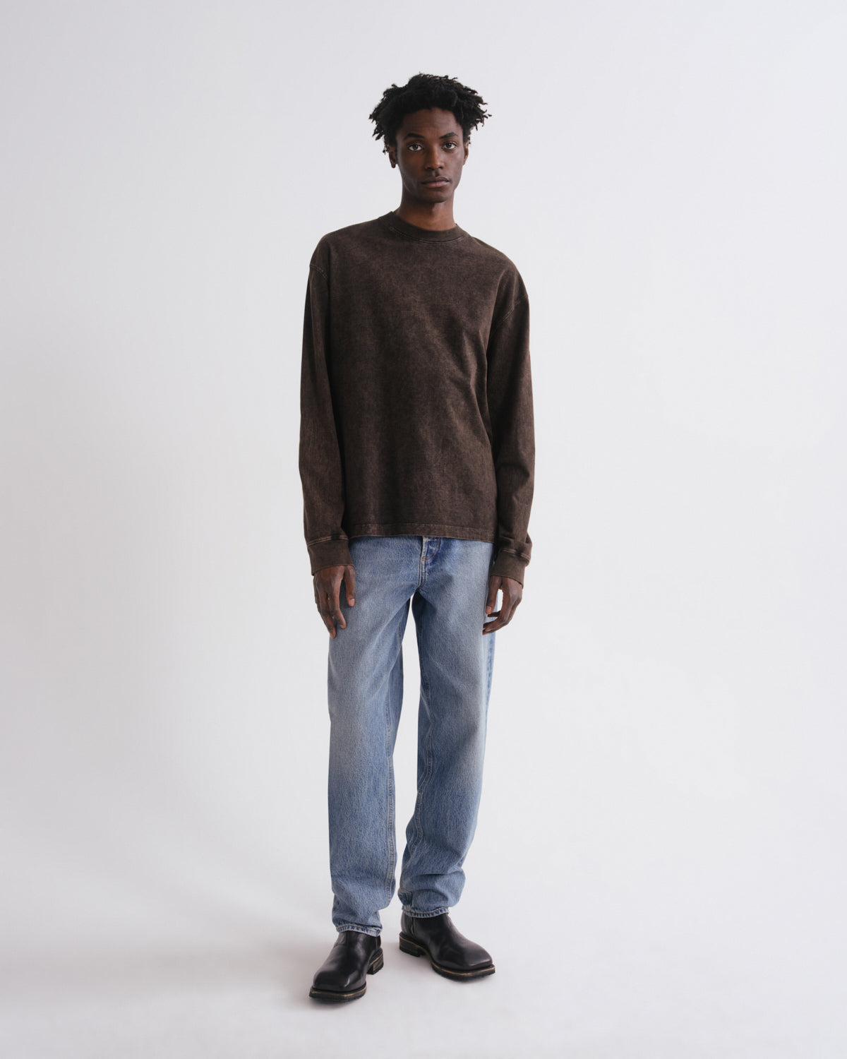 Man wearing a brown sweater and blue jeans on a white background