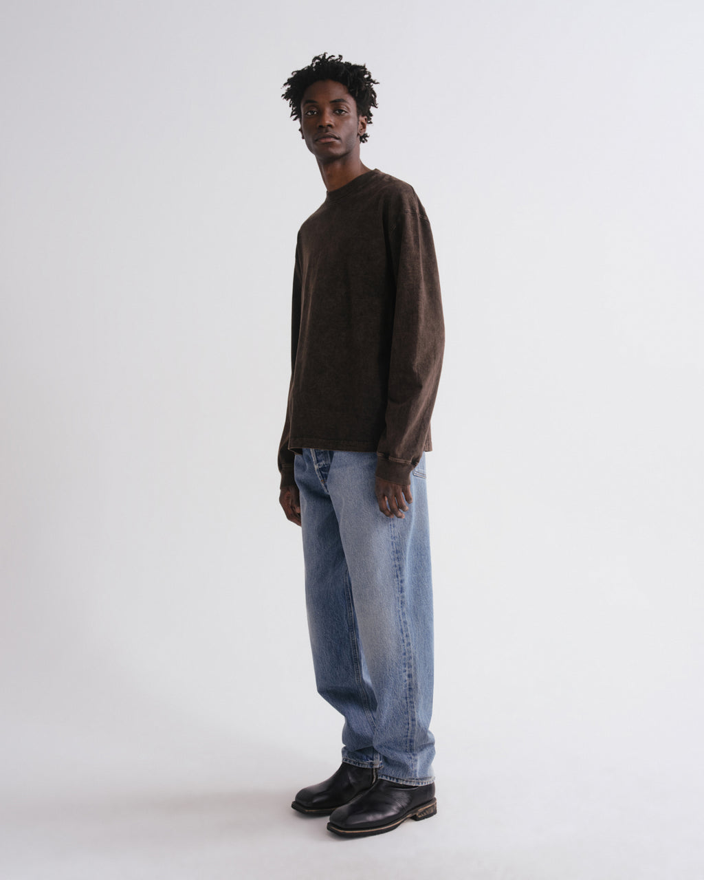 Person wearing a brown sweater, blue jeans, and black shoes on a white background
