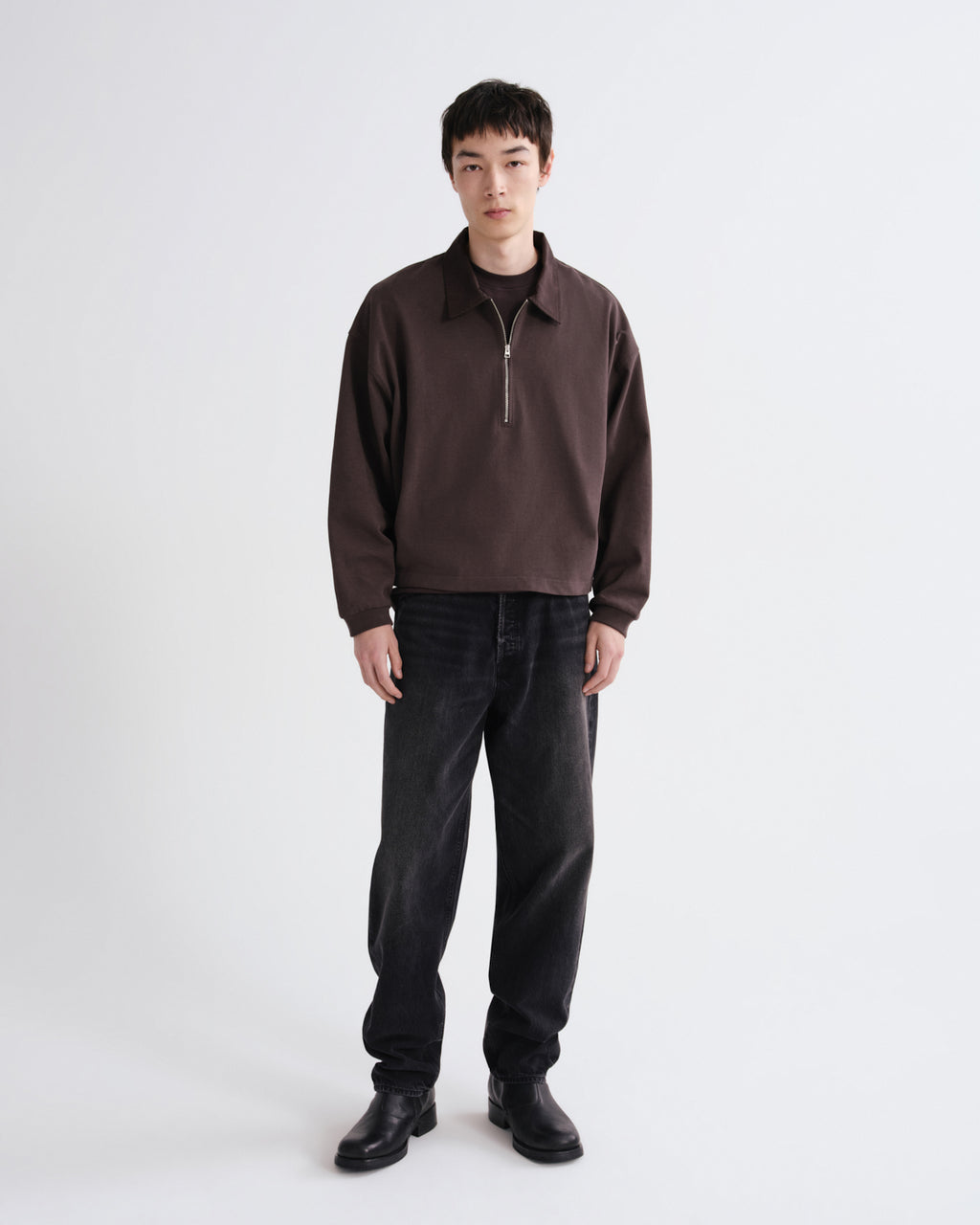 Person wearing a brown sweater and black pants on a white background