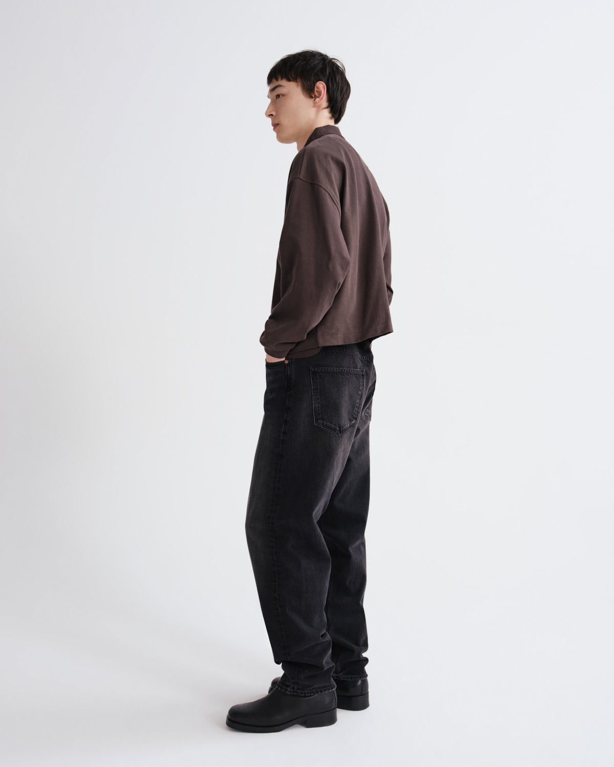Person wearing a brown shirt and black pants standing against a white background