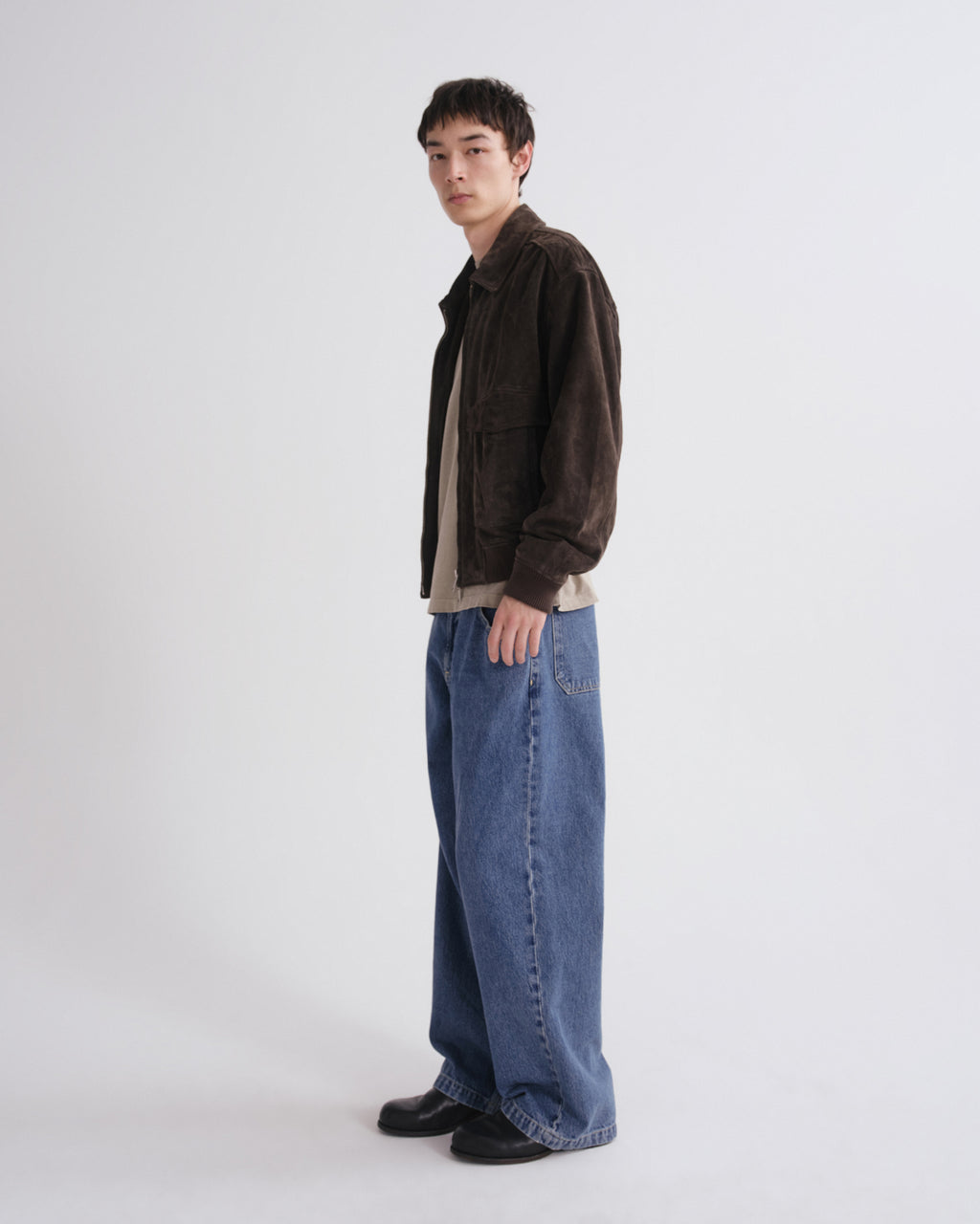Person wearing a brown jacket and blue jeans on a grey background
