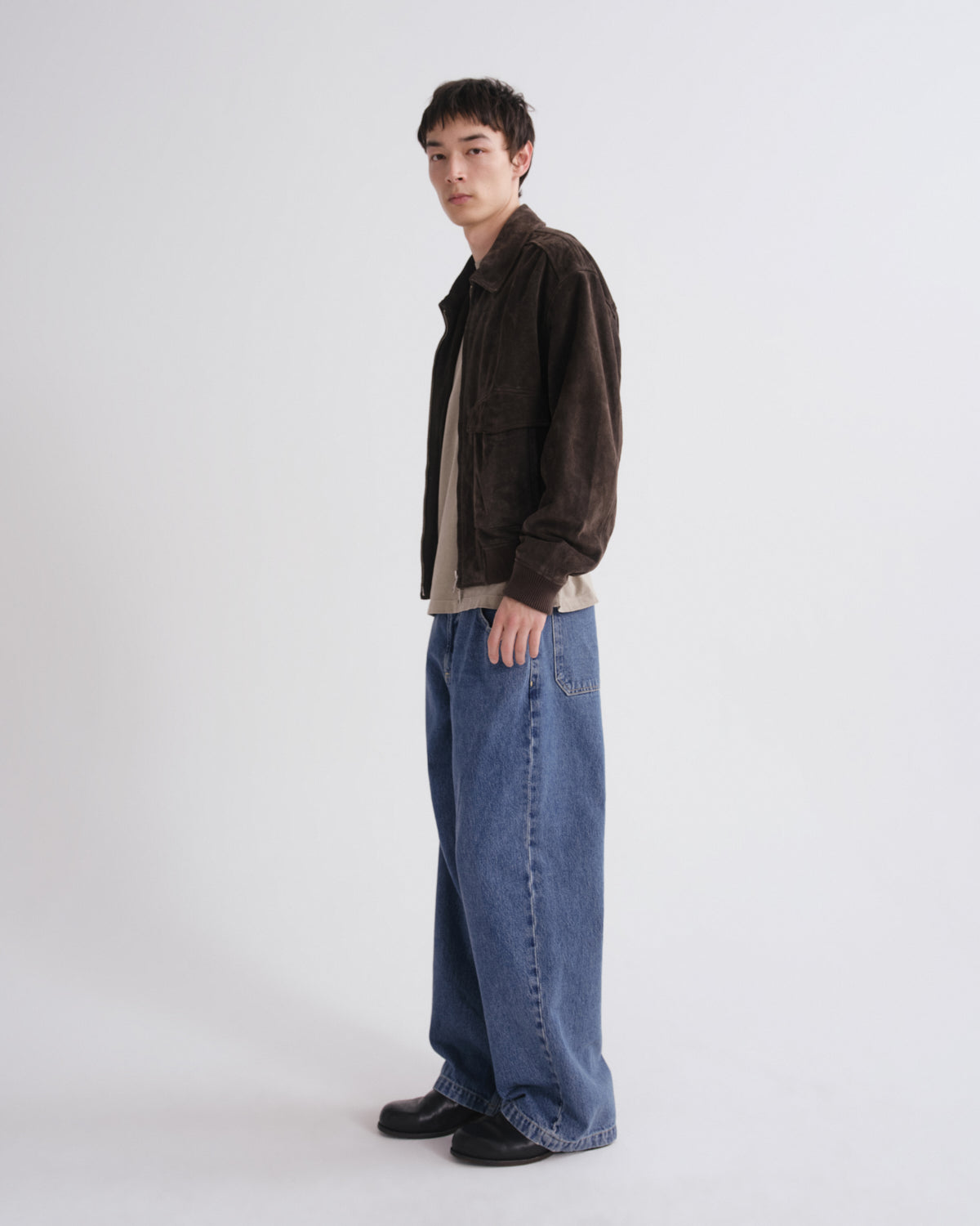 Person wearing a brown jacket and blue jeans on a grey background
